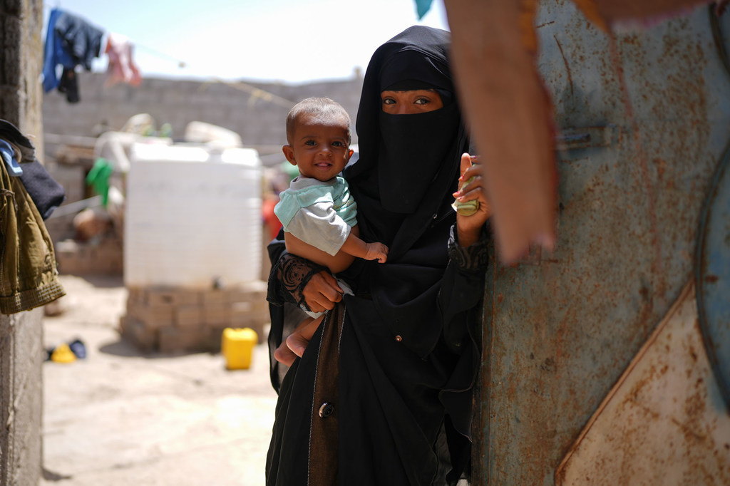 أم تحمل طفلها بالقرب من منزلهما في حي العدني بمدينة الحوطة في اليمن.